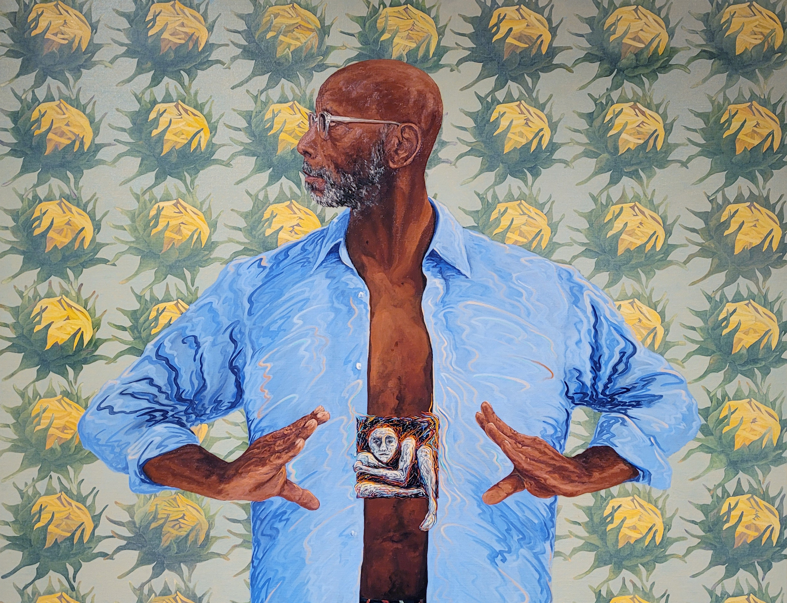 Painting with a flat appearance on a background of green with rows of yellow and green flowers. In the center is a man in an open blue shirt holding his hands near his chest, looking to the right.