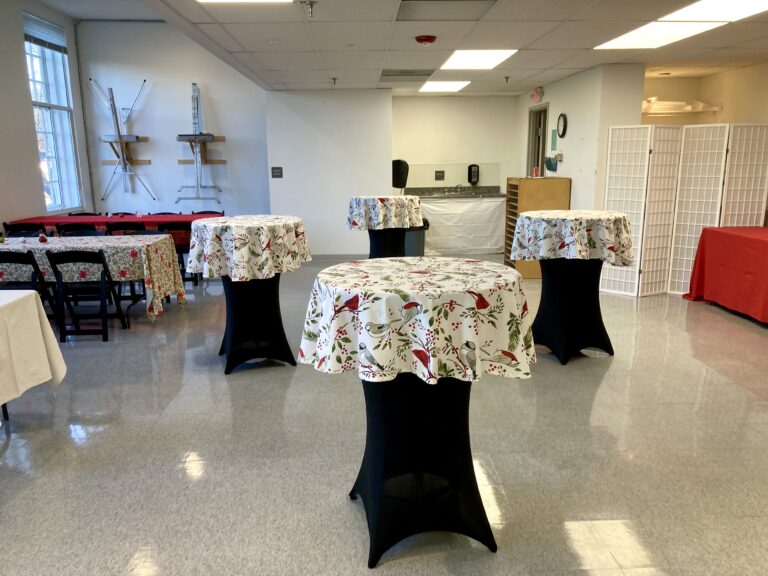 Photograph of a room with white walls with rectangular tables to the far left and round tables in the center.